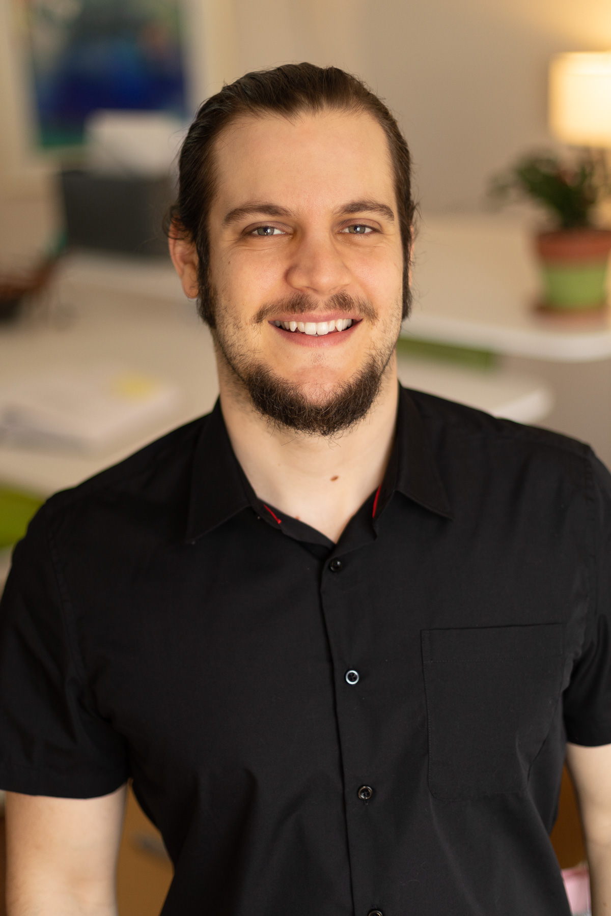 A young male professional videographer at Circuit Media, smiling and wearing a black short sleeve button up