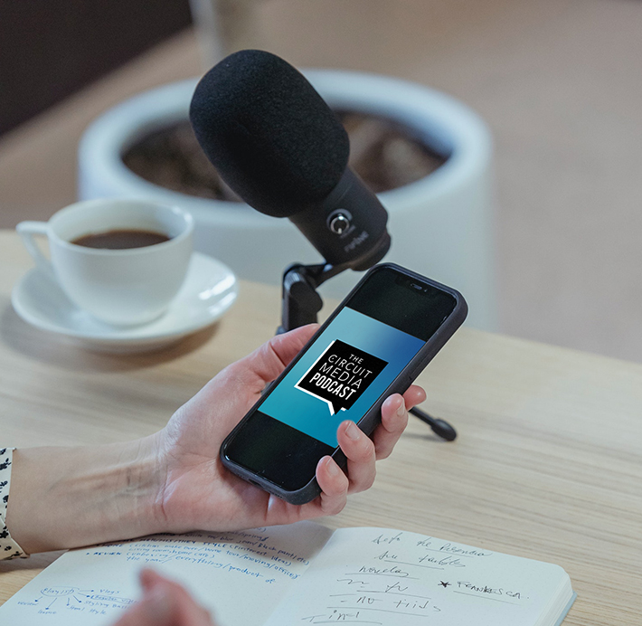 A microphone next to a hand holding a phone with the Circuit Media Podcast logo