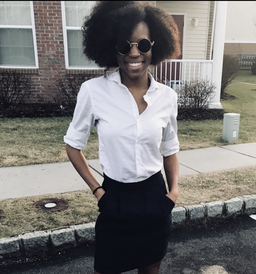 Circuit Media's new project manager and government contracts teammate Clarissa Mitchell is standing near a sidewalk smiling. She has her hands in her pockets and sunglasses on.