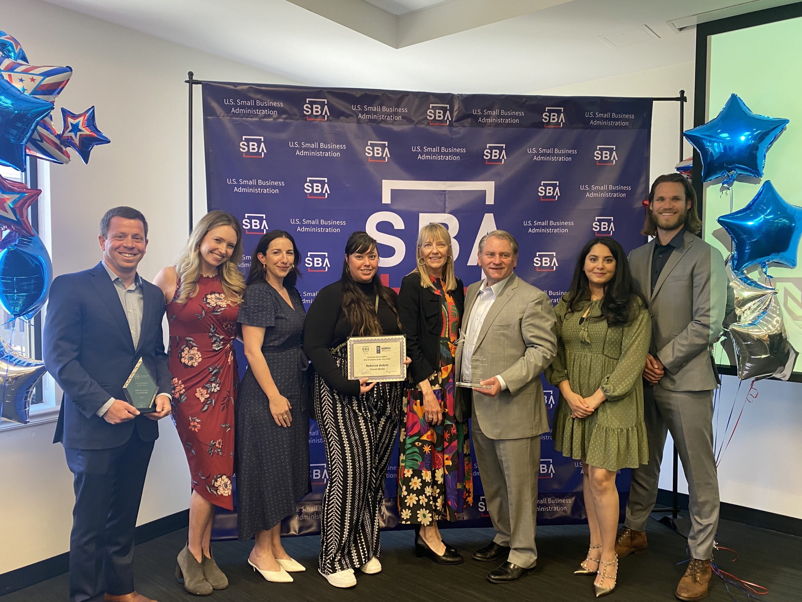 From left to right: Nick Eckerman, Ali Manor, Lisa McKell, Jess Brovsky-Eaker, Rebecca Askew, Dean Morton, Anoud Saeed, and Jacob Hurley. The team is accepting the Regional and 8(a) Graduate of the Year awards at the SBA small business awards ceremony.